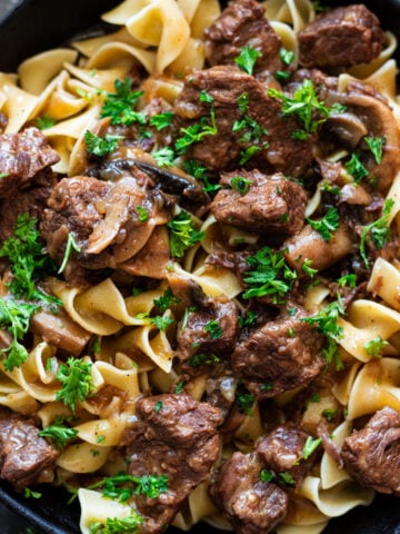 Close up of beef tip over egg noodles topped with parsley.