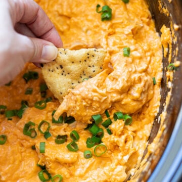 Person scooping buffalo chicken dip with chip.