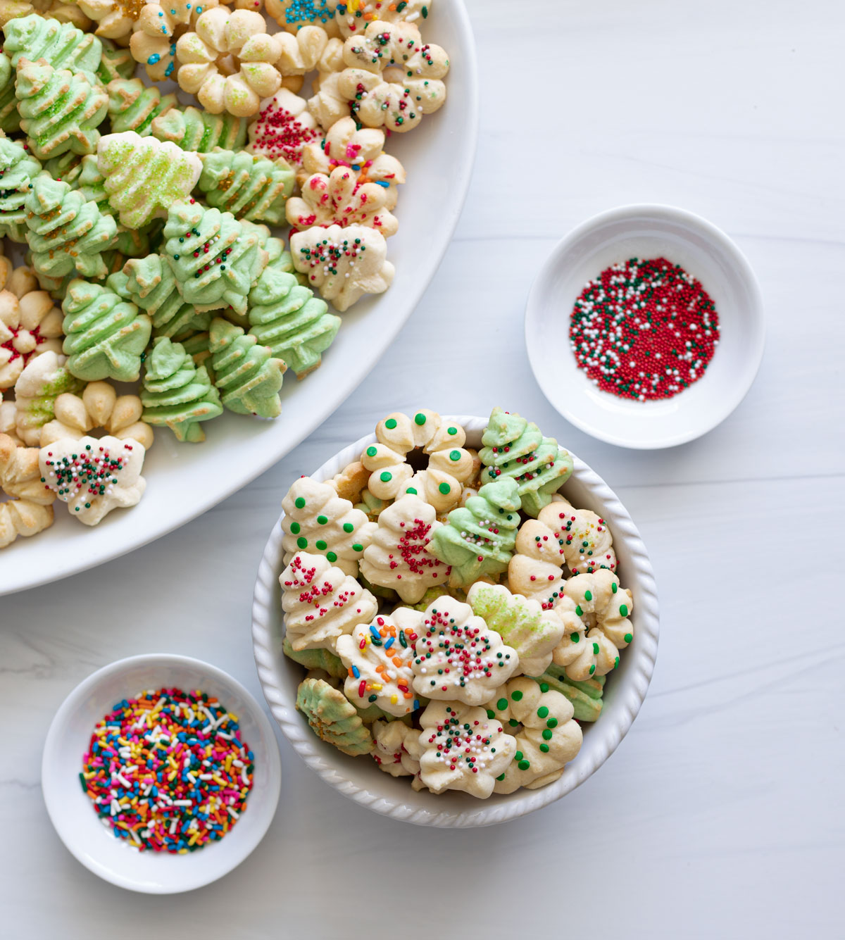 A bowl of spitz cookies next to a platter and bowls of sprinkles. 