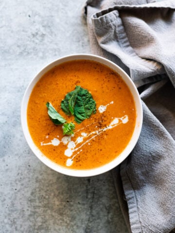 Bowl of roasted red pepper soup topped with cream and basil.