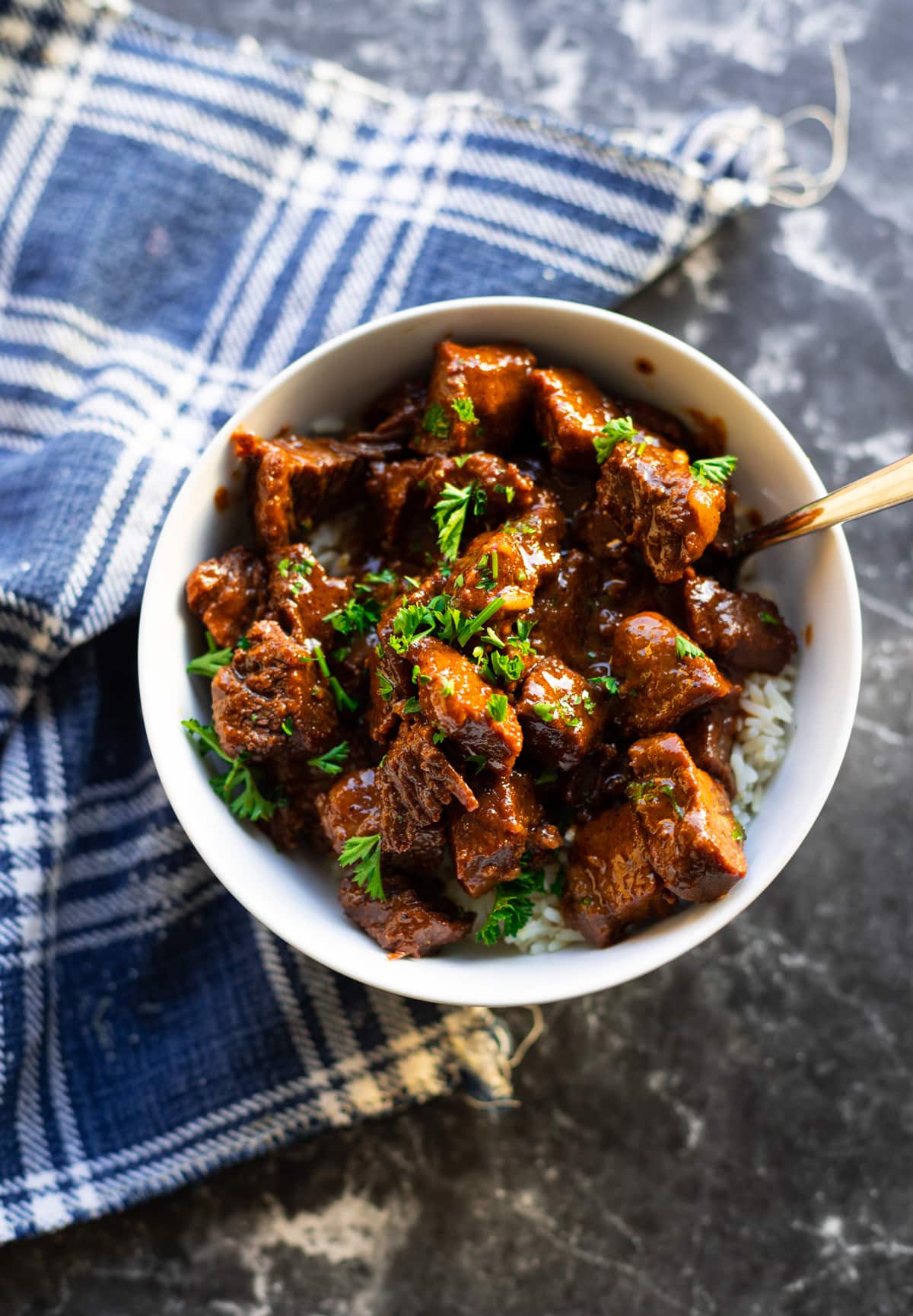 Top down view of a bowl of steak bites  in a bowl of rice, topped with parsley. 