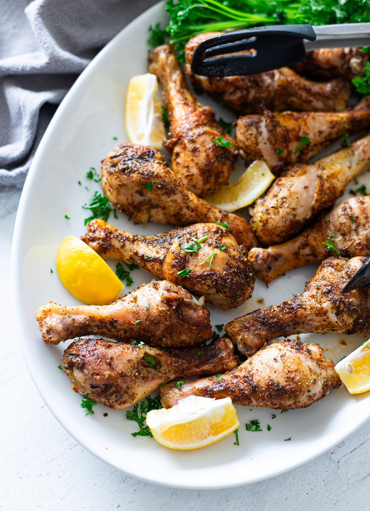 Browned and crispy baked chicken legs on a serving platter with lemon wedges. 