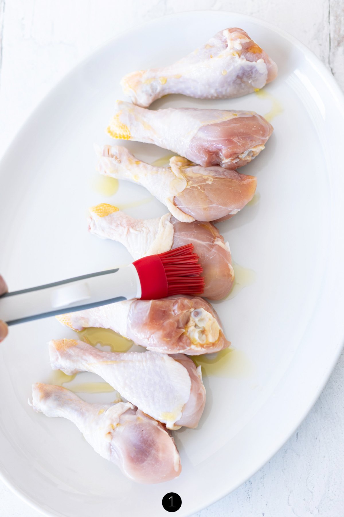 Person basting olive oil over chicken legs.