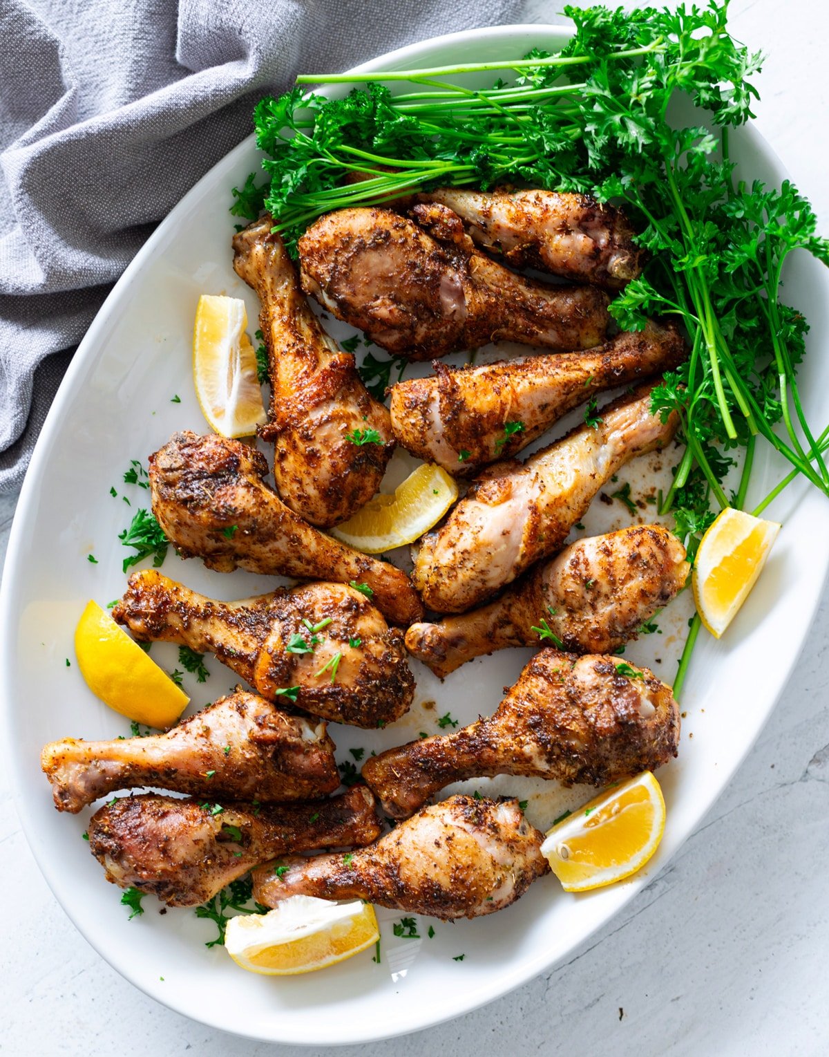 Browned and crispy baked chicken legs on a serving platter with lemon wedges and parsley sprigs. 