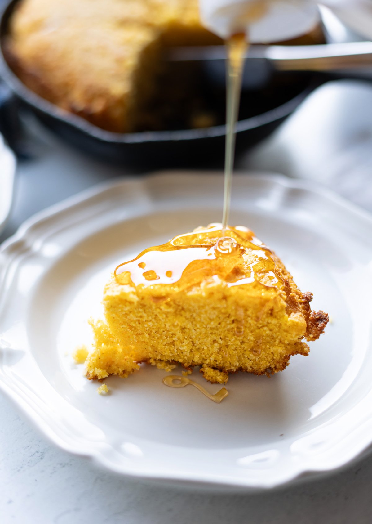 Honey being drizzled over a piece of cornbread. 