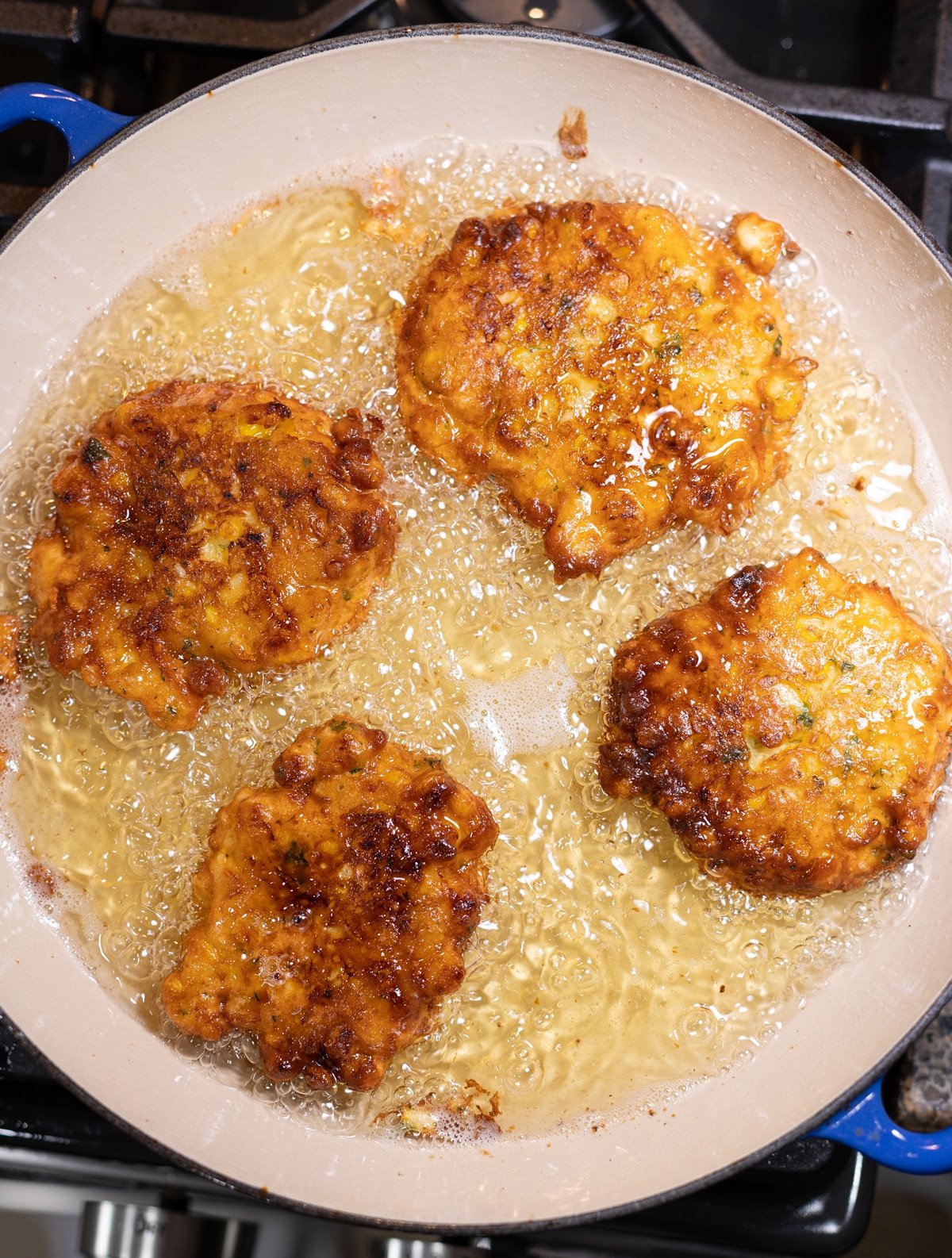 Deep frying corn fritters in a pan of oil. 