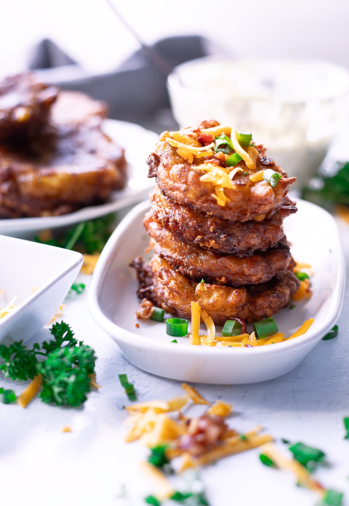 Corn fritters stacked on a serving dosh topped with cheese and bacon. 
