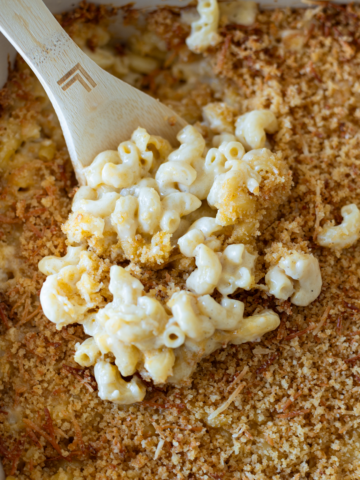 Person spooning a large portion of mac and cheese from a casserole dish.