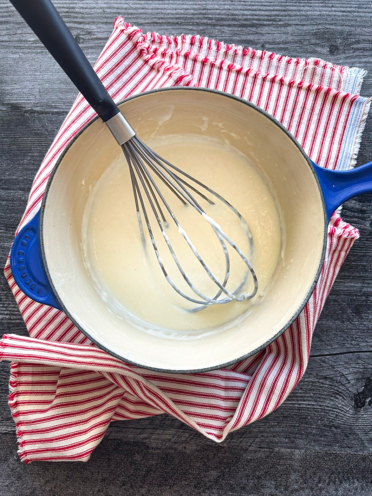 A sauce pan filled with Béchamel Sauce Recipe with a whisk on the side.