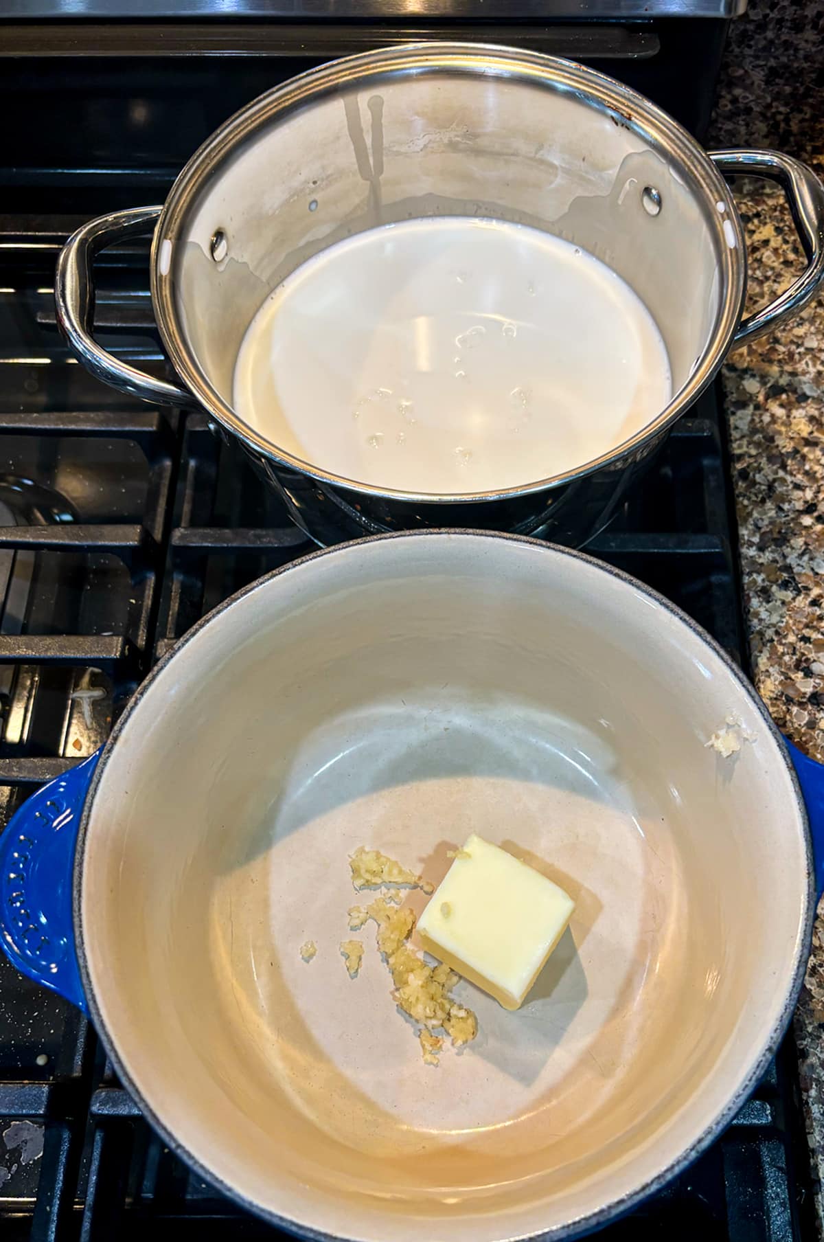 Person melting butter and minced garlic in a saucepan and warming milk in a separate pan.