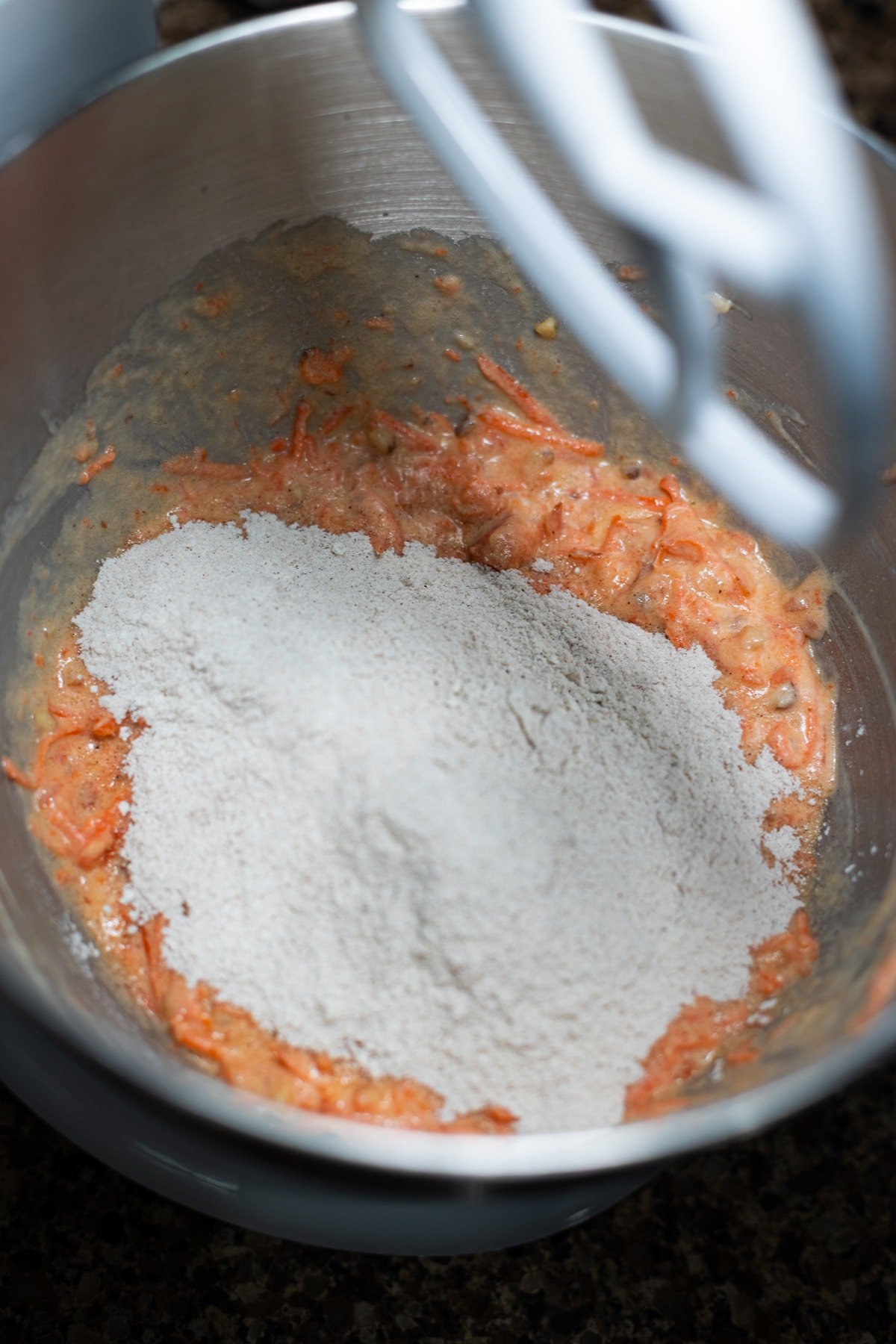 Wet ingredients in a bowl and person adding in dry ingredients. 